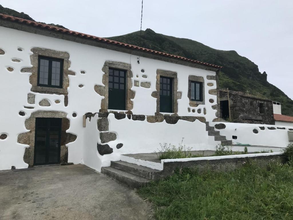 a white building with a hill in the background at A casa do Tí Mendonça in Lajes das Flores