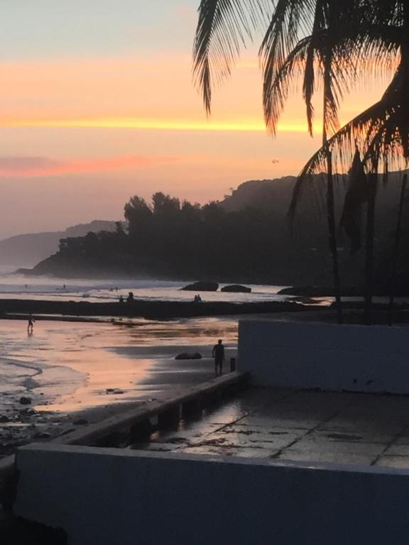 a sunset over a beach with palm trees and the ocean at Looking Good Beachfront Hotel in El Zonte