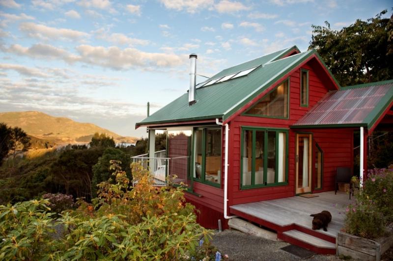 una casa roja con un perro sentado en un porche en Hereweka Garden Retreat, en Dunedin