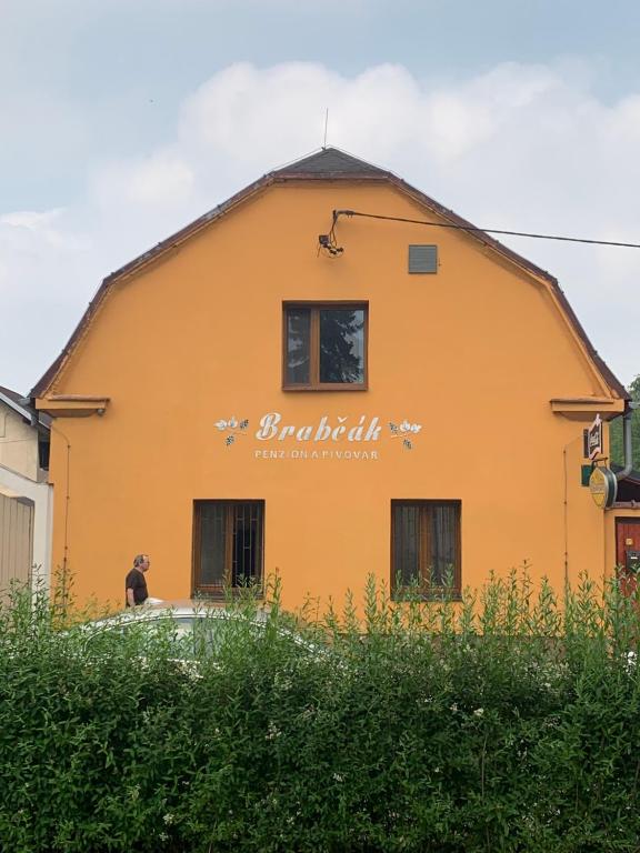 Ein orangefarbenes Gebäude mit einer Frau, die davor steht. in der Unterkunft Penzión Brabčák in Vratimov