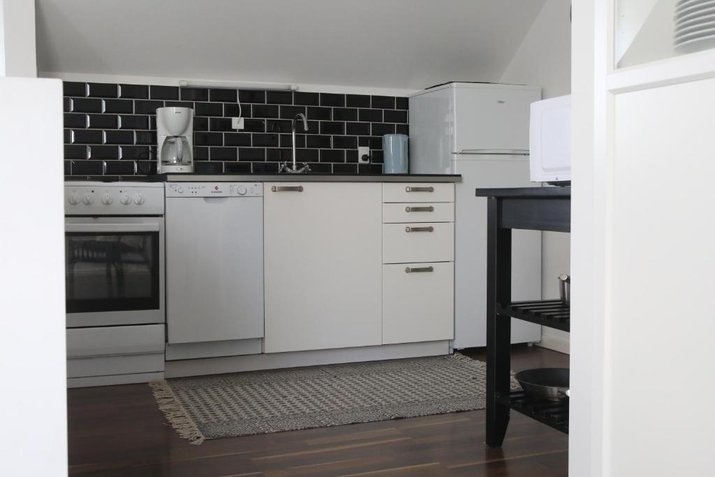 a kitchen with white appliances and a black tile wall at Dragondrum Bed & Kitchen in Ullerslev