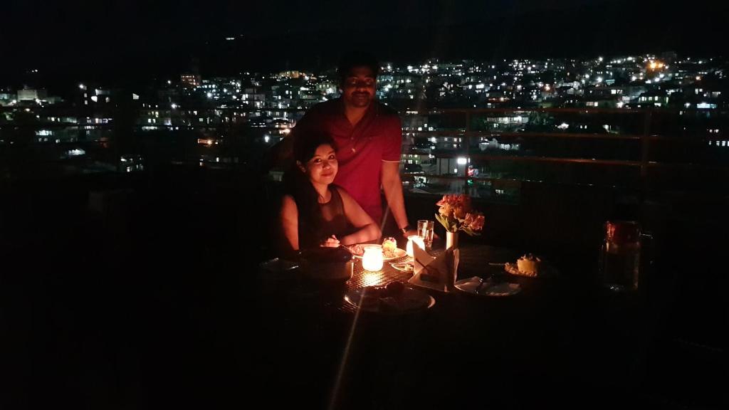 a man and a woman standing on a balcony at night at Woodland Hill Stay in Shillong