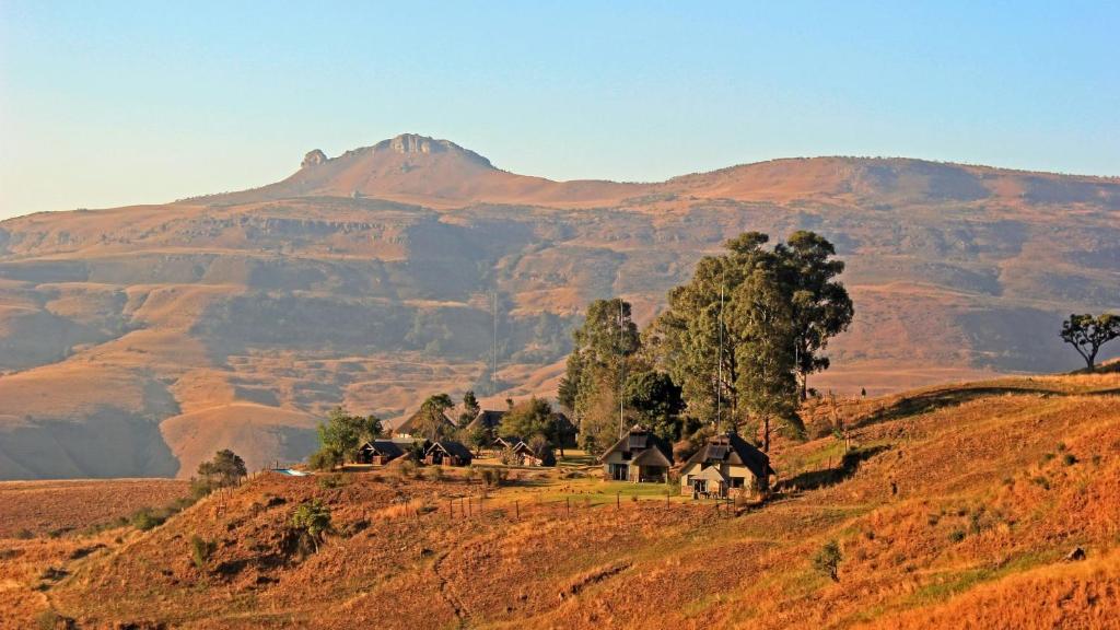 a group of houses on a hill with mountains in the background at Sungubala Eco Camp in Bergville