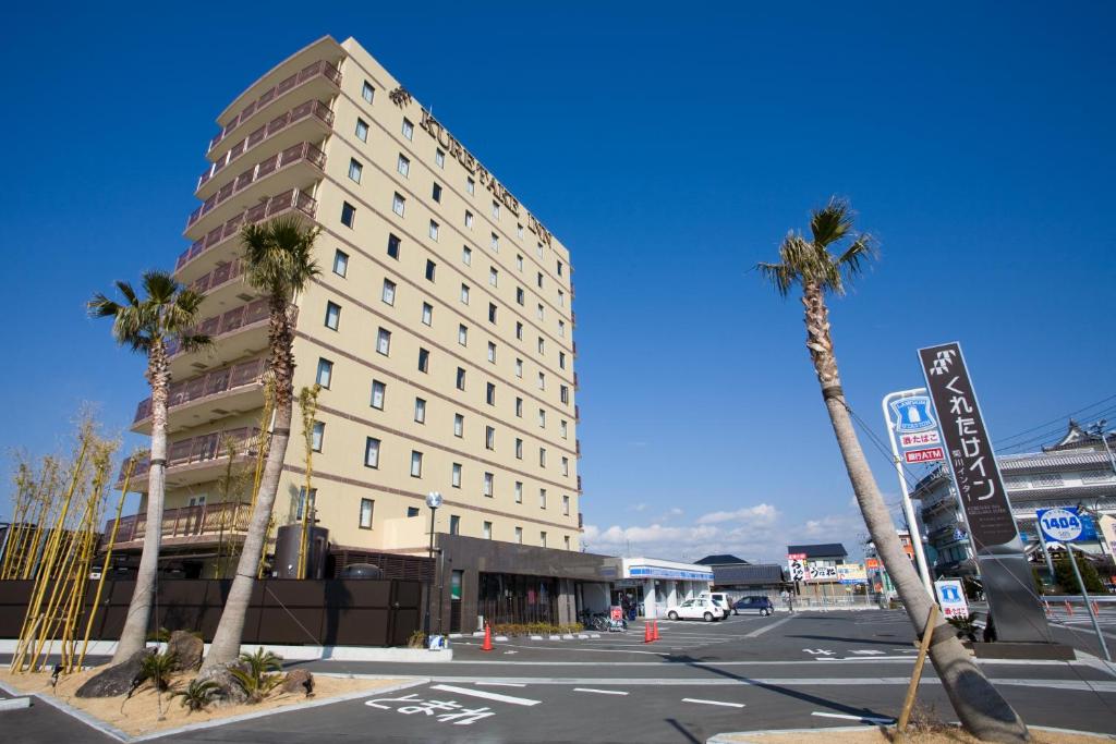 a tall building with palm trees in front of a street at Kuretake-Inn Kikugawa I.C. in Kikugawa