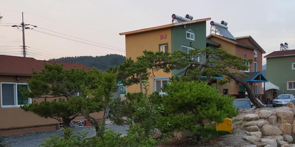 un edificio amarillo y verde con árboles delante de él en Wind Come Pension Gyeongju, en Gyeongju