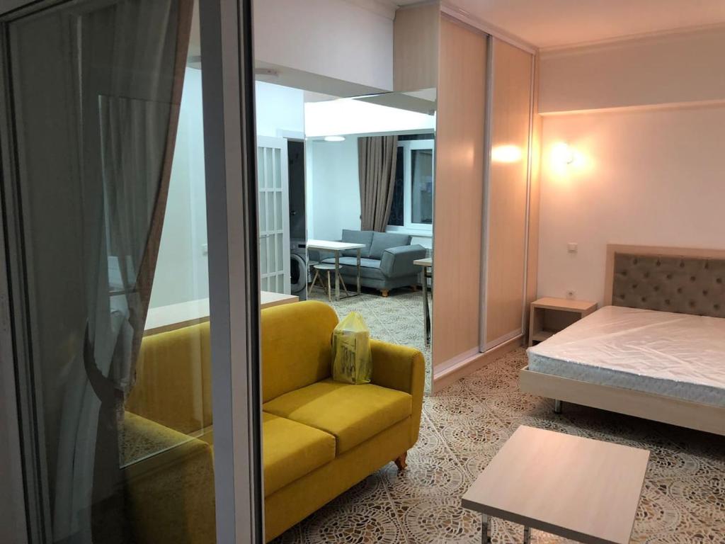 a living room with a yellow couch and a bedroom at Студия в центре Ташкента in Tashkent