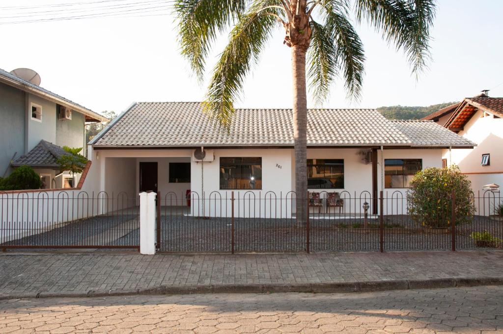 une clôture devant une maison avec un palmier dans l'établissement Melhor Casa para locação em Pomerode, à Pomerode