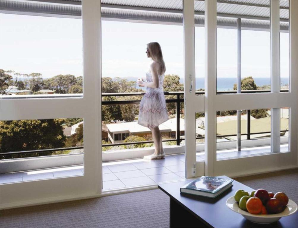 een vrouw op een balkon met uitzicht op de oceaan bij Horizon Holiday Apartments in Narooma