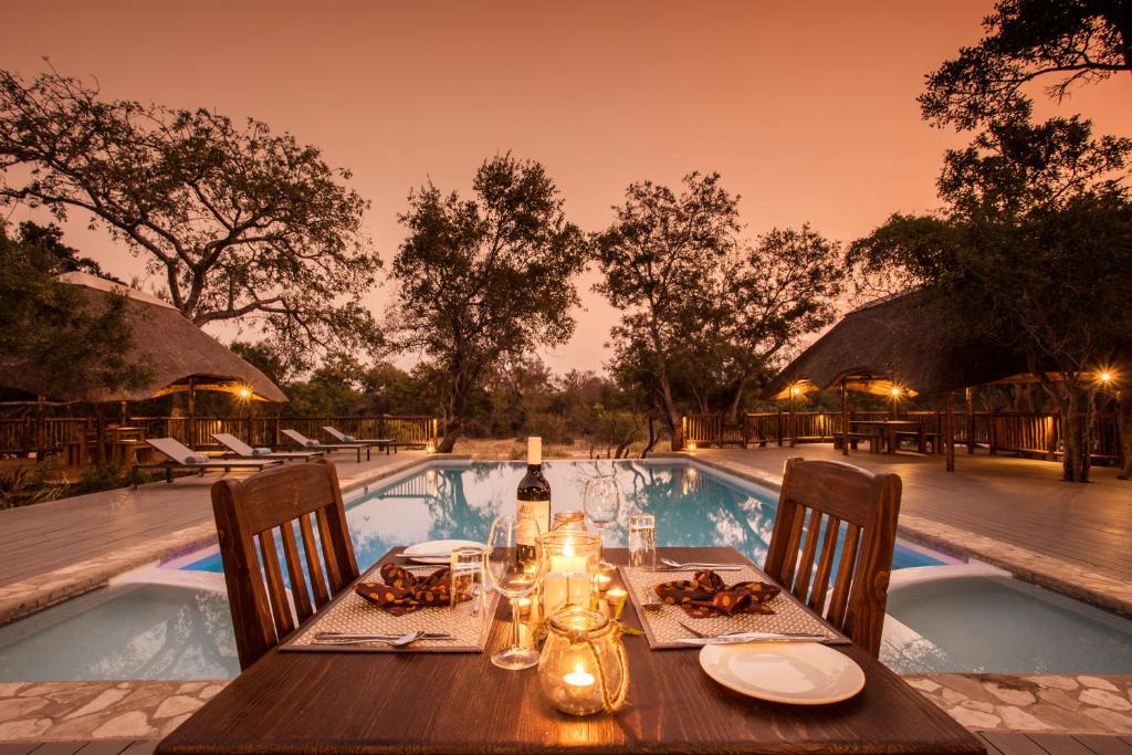 a table with a bottle of wine on it next to a swimming pool at Vuyani River Lodge in Hoedspruit