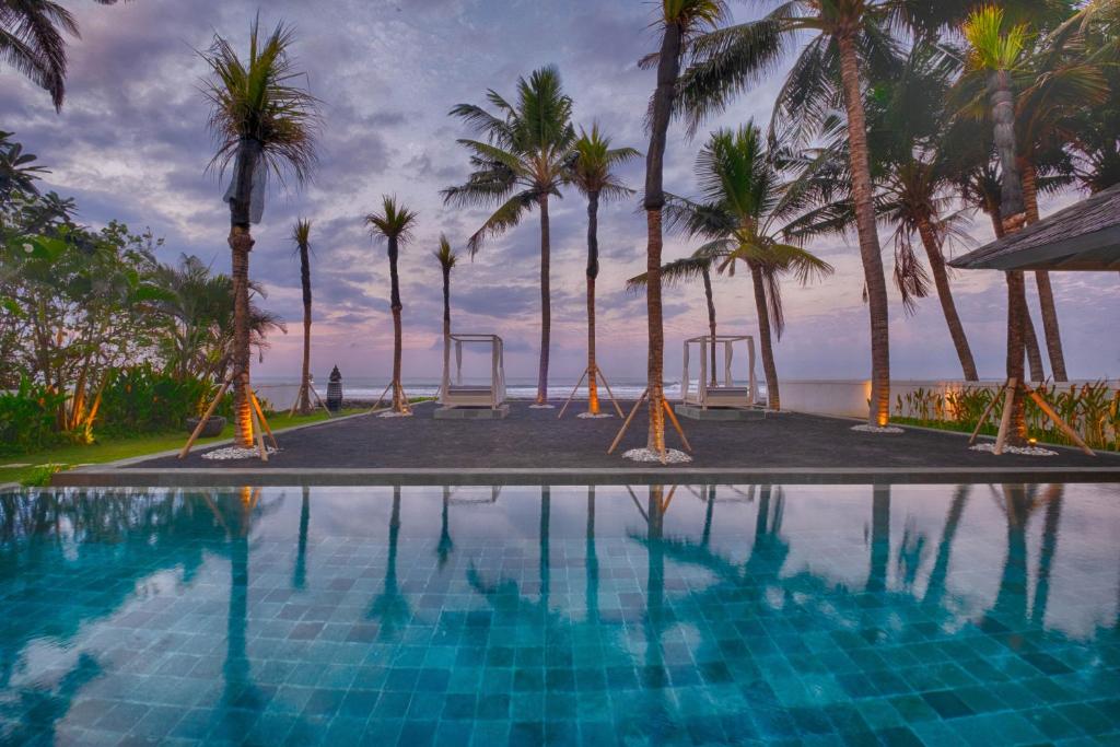 a swimming pool with palm trees and the ocean at Kutus Kutus Saba Beach Villa in Gianyar