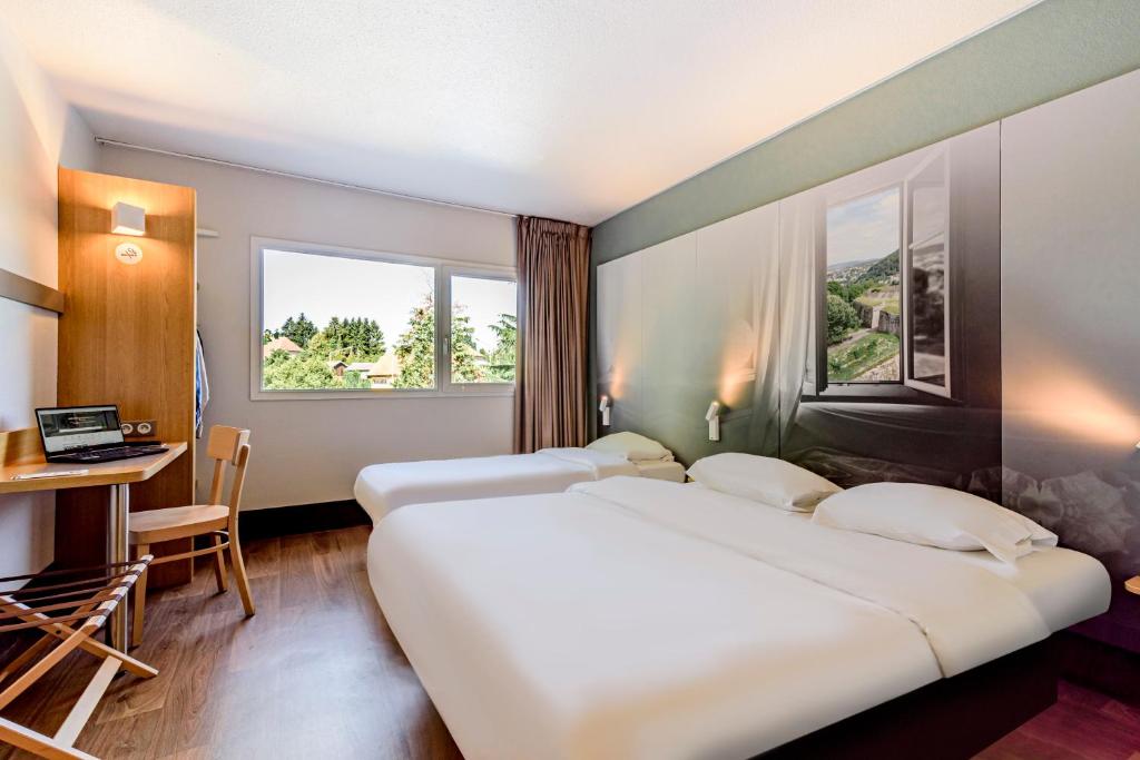 a hotel room with two beds and a desk and window at B&B HOTEL Besançon Chateaufarine in Besançon