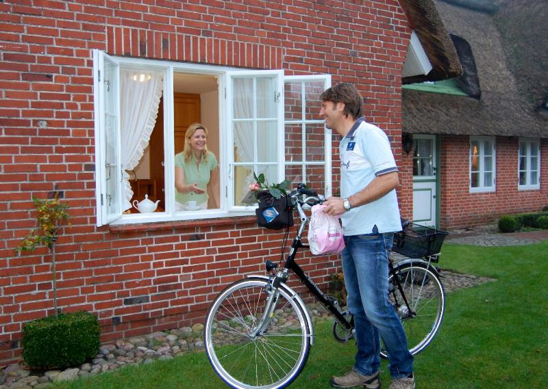 een man die met een fiets voor een huis staat bij Reetdachhus an de Diek in Sankt Peter-Ording