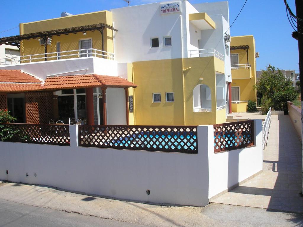 una casa amarilla y blanca con una valla en Dimitra Apartments, en Gouves