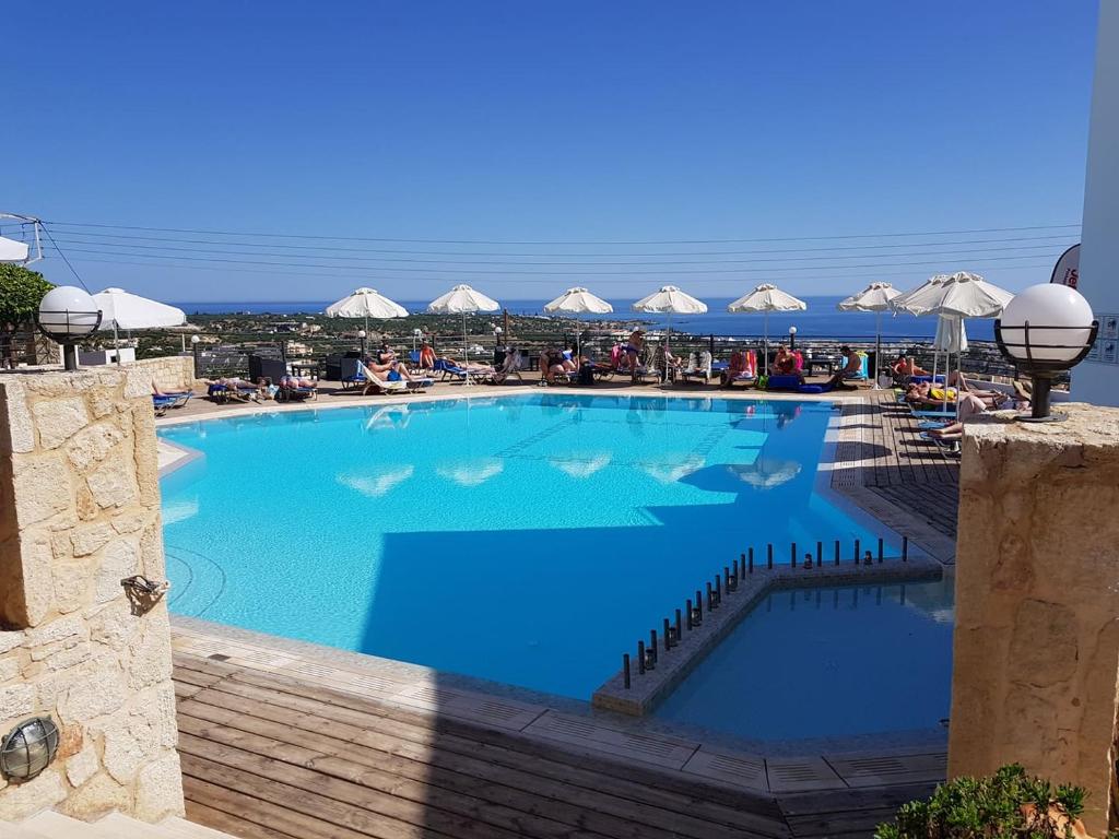 una gran piscina azul con sillas y sombrillas en Amazones Village Suites en Hersonissos