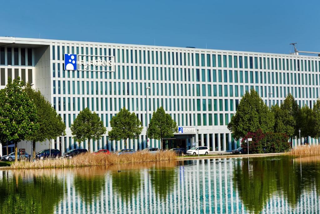 a large white building with a reflection in a body of water at H2 Hotel München Messe in Munich