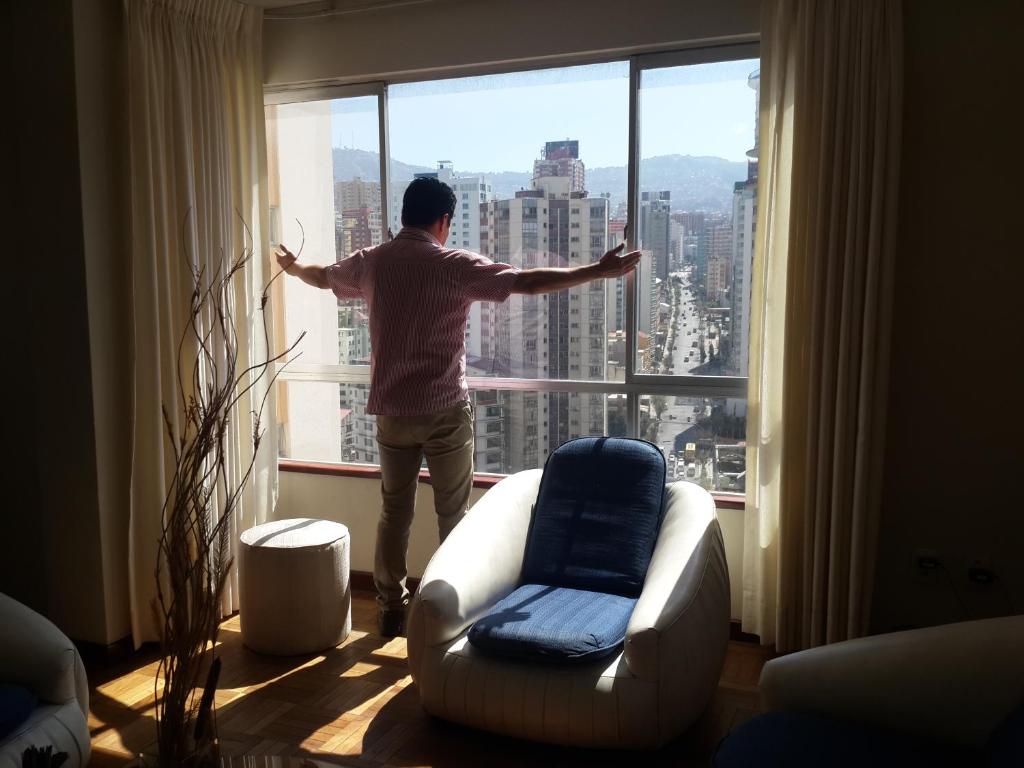 un hombre parado en una ventana mirando a la ciudad en APARTAMENTO PRIVADO Piso 20a, CENTRICO, CERCA EMBAJADA USA, TELEFERICO, MALLS, VISTAS 360 y ZONA SEGURA en La Paz