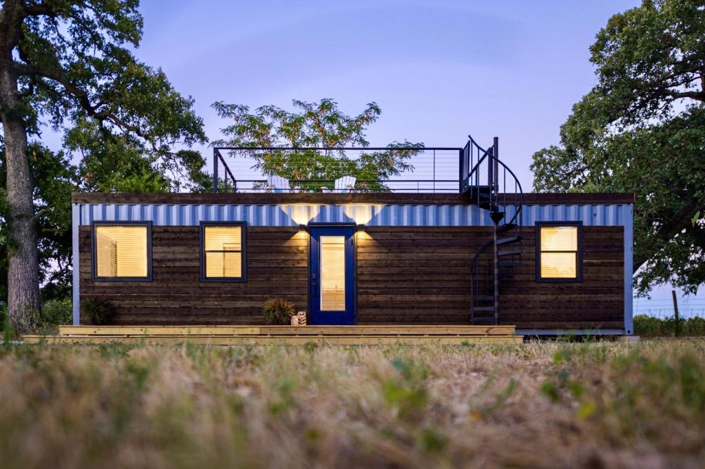 a small house with lights on in a field at The Shoreline Container Home 12 min to Magnolia Silos and Baylor in Waco