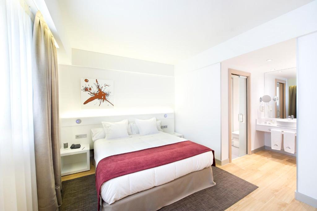 a white bedroom with a large bed and a bathroom at Sercotel Ciudad de Miranda in Miranda de Ebro