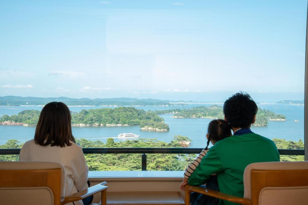 a group of three people sitting on a balcony overlooking a river at Hotel Matsushima Taikanso in Matsushima