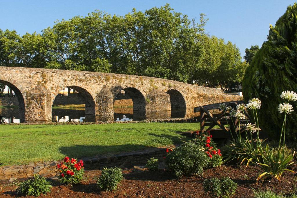 uma ponte de pedra com arcos num parque com flores em Convento Da Serta Hotel na Sert