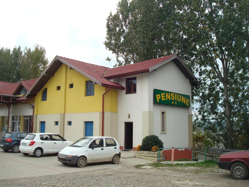 un bâtiment jaune et blanc avec des voitures garées dans un parking dans l'établissement Pensiunea Marc, à Suceava