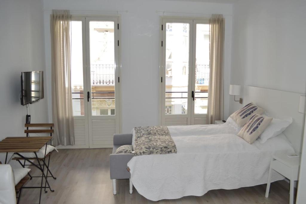 a white bedroom with a bed and a chair at Modern studio flat close to Plaza Merced in Málaga