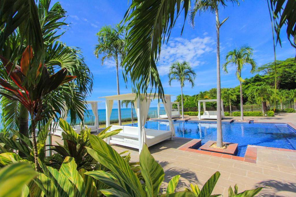 a resort swimming pool with palm trees and the ocean at 2201 Playa EL Palmar in Las Palmeras