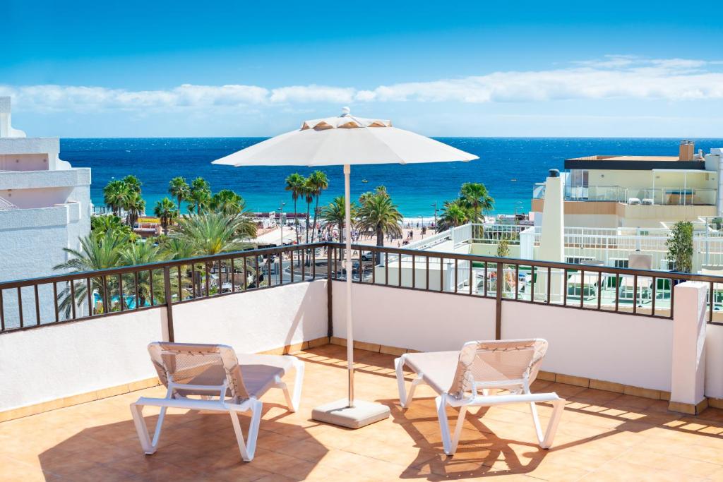 einen Balkon mit 2 Stühlen, einem Sonnenschirm und dem Meer in der Unterkunft Apartamentos las Góndolas in Playa del Ingles