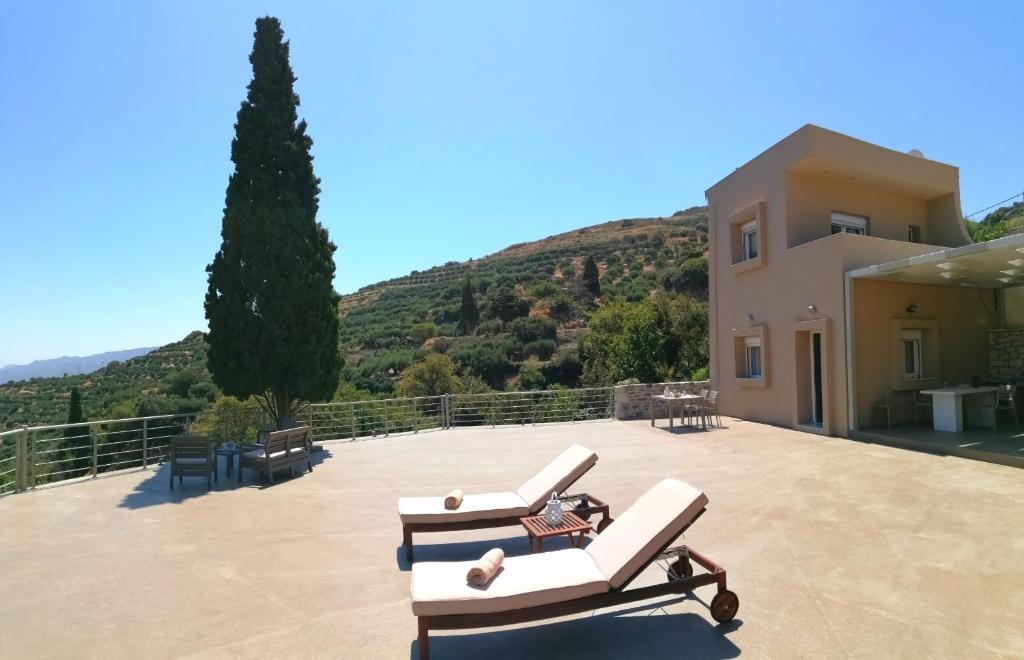 a patio with two lounge chairs and a house at Villa Irini - Cretan Luxury Villa with Amazing View in Paraspórion