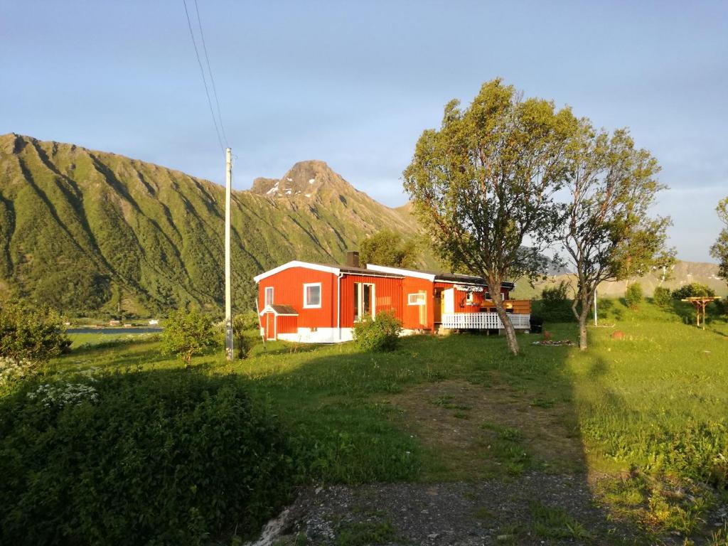 a red house in a field with mountains in the background at Midnattsolveien 3158,Sommarhusstrand in Laukvik