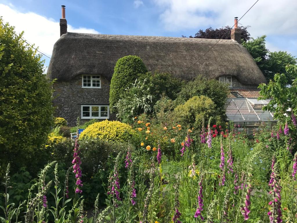 un cottage con il tetto di paglia e un giardino con fiori di Corner House a Cudworth