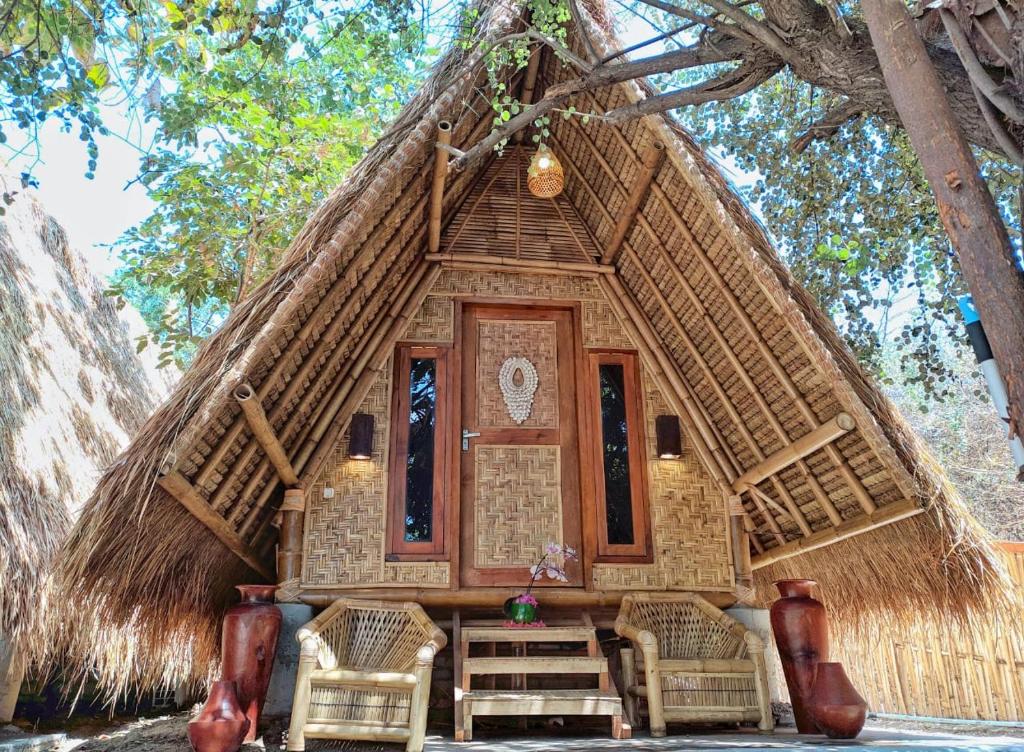 una casa con techo de paja con sillas y mesa en Gili Kampoeng en Gili Trawangan