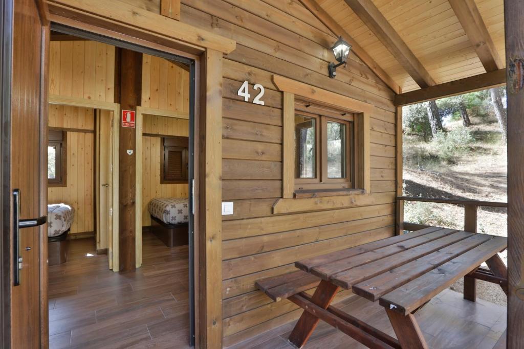 a wooden cabin with a bench on the porch at Complejo Residencial Los Enebros in Arroyo Frio