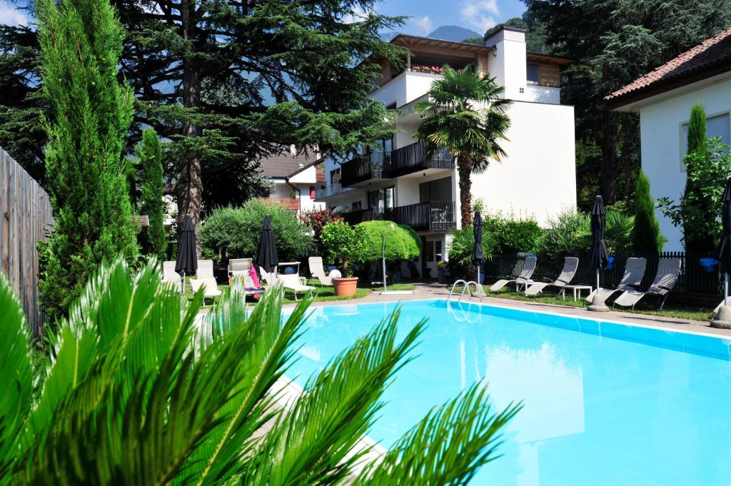 a swimming pool in front of a building with chairs and trees at Hotel Jasmin in Merano