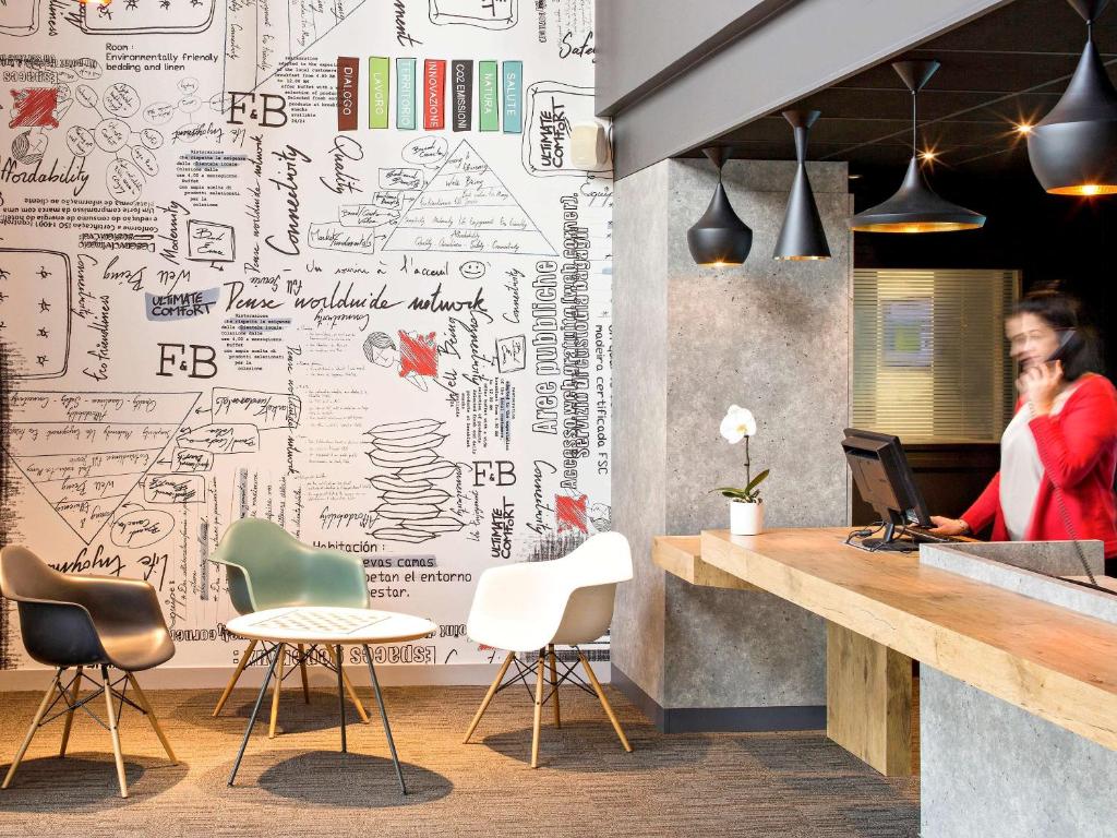 a woman talking on a cell phone in a office with a wall covered in drawings at ibis Clermont Ferrand Montferrand in Clermont-Ferrand