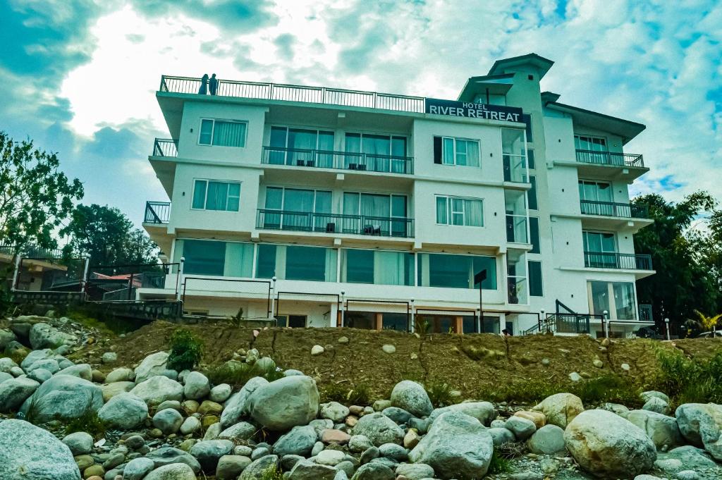 a building on a hill next to a pile of rocks at Hotel River Retreat in Kangra