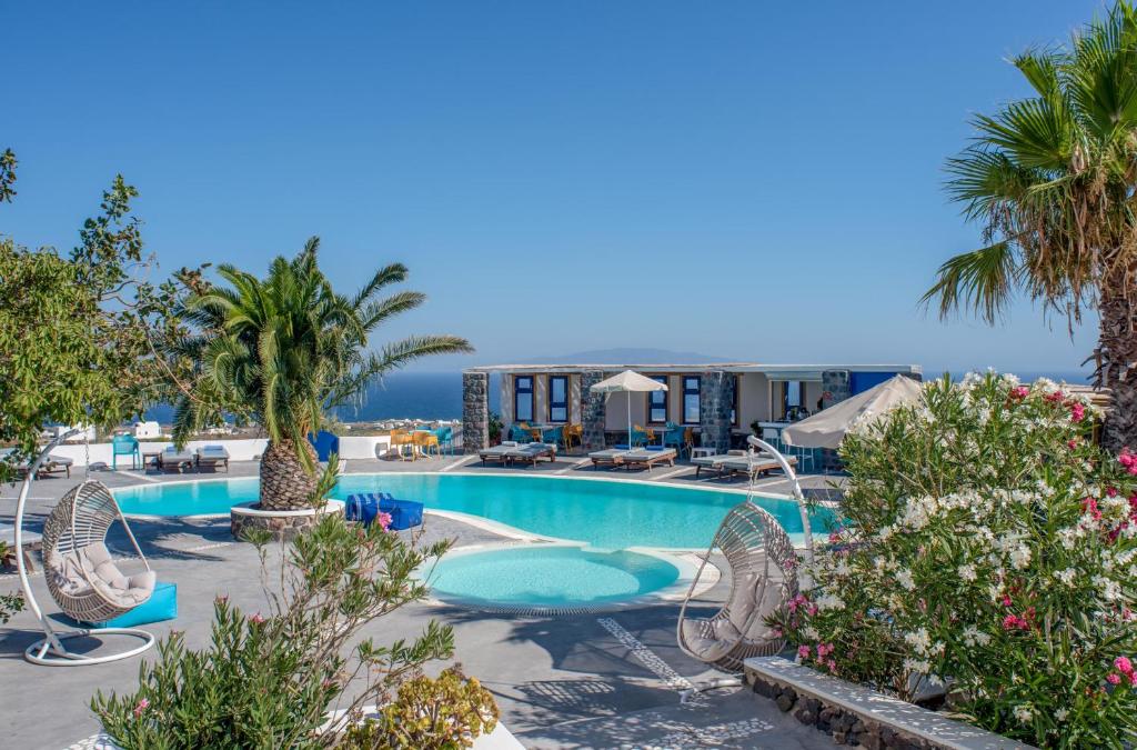 a large swimming pool with chairs and palm trees at Anemomilos in Oia