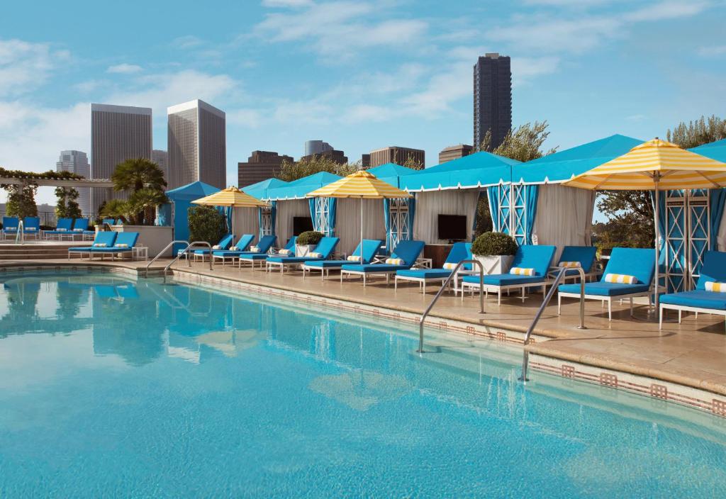 a swimming pool with blue chairs and umbrellas at The Peninsula Beverly Hills in Los Angeles