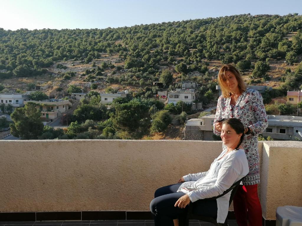 two women sitting on the edge of a ledge with a view at Mhna guest house in Ajloun