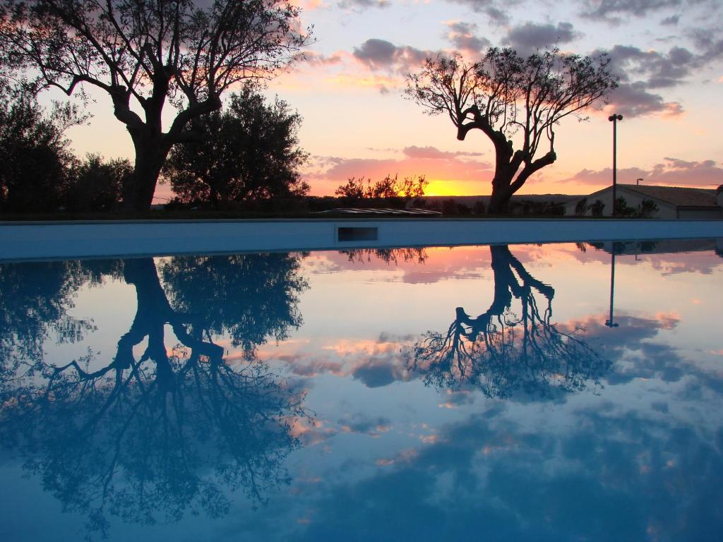 une réflexion sur les arbres d'une piscine au coucher du soleil dans l'établissement Kinanto Bioresort, à Ispica