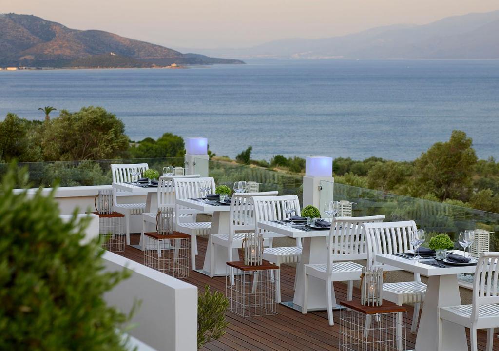 a row of white tables and chairs on a deck with the ocean at Proteas Blu Resort in Pythagoreio