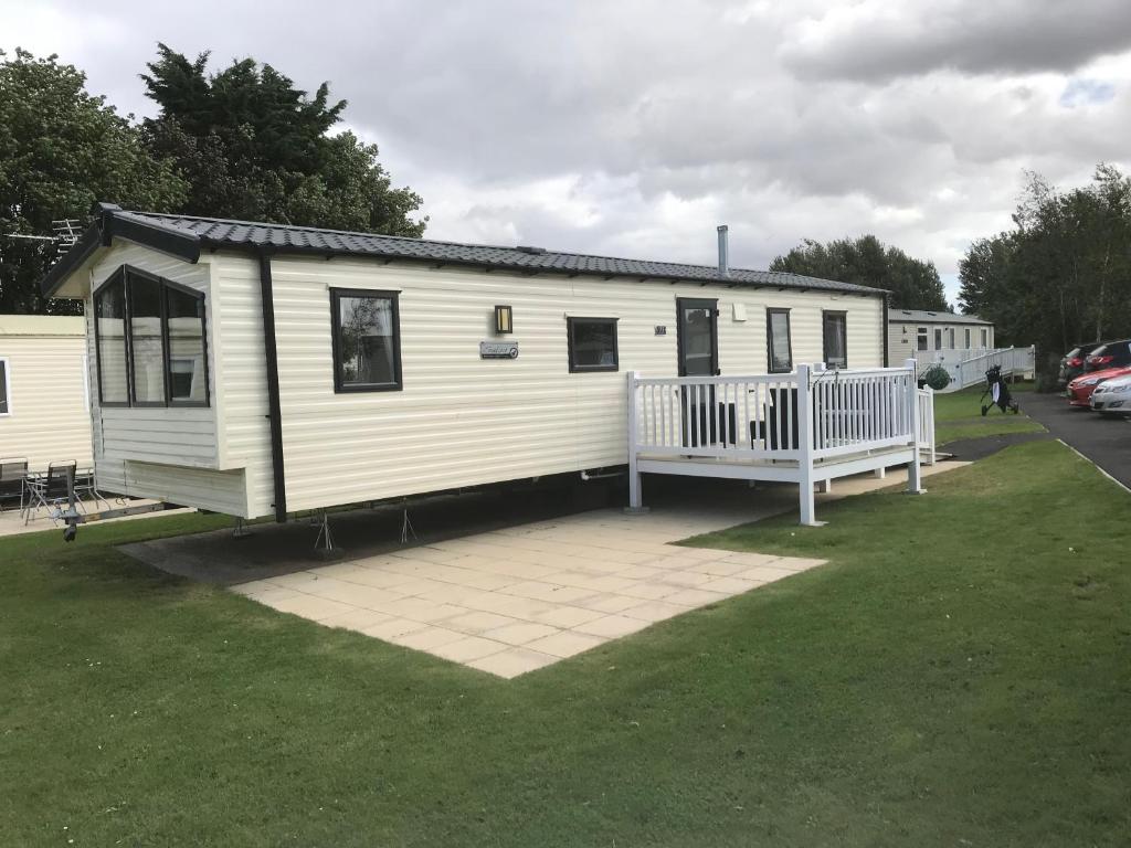 3 bedroom deluxe caravan في Longniddry: منزل متنقل أبيض مع شرفة على ساحة