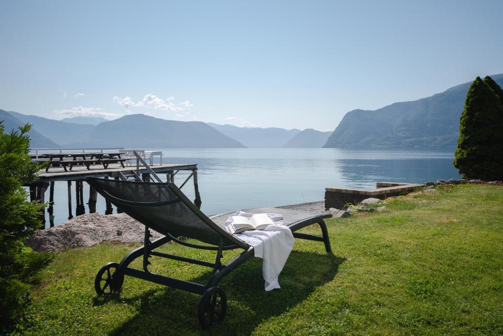 un banco sentado en la hierba junto a un cuerpo de agua en Leikanger Fjordhotel - Unike Hoteller, en Leikanger