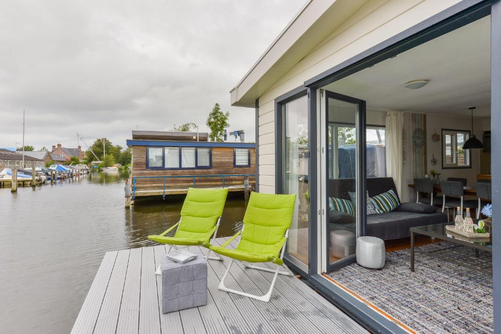 a house with two green chairs on a dock next to the water at Bright and Comfortable Houseboat in Aalsmeer