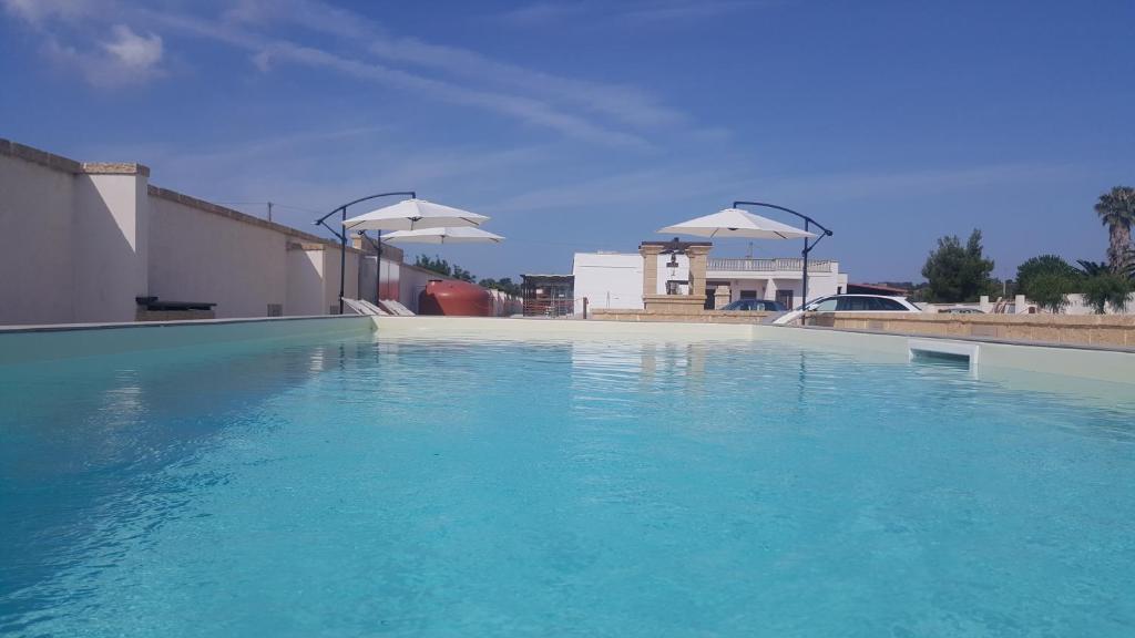 una gran piscina de agua azul con dos sombrillas blancas en Villa Silvia Luxury Residence, en Taviano