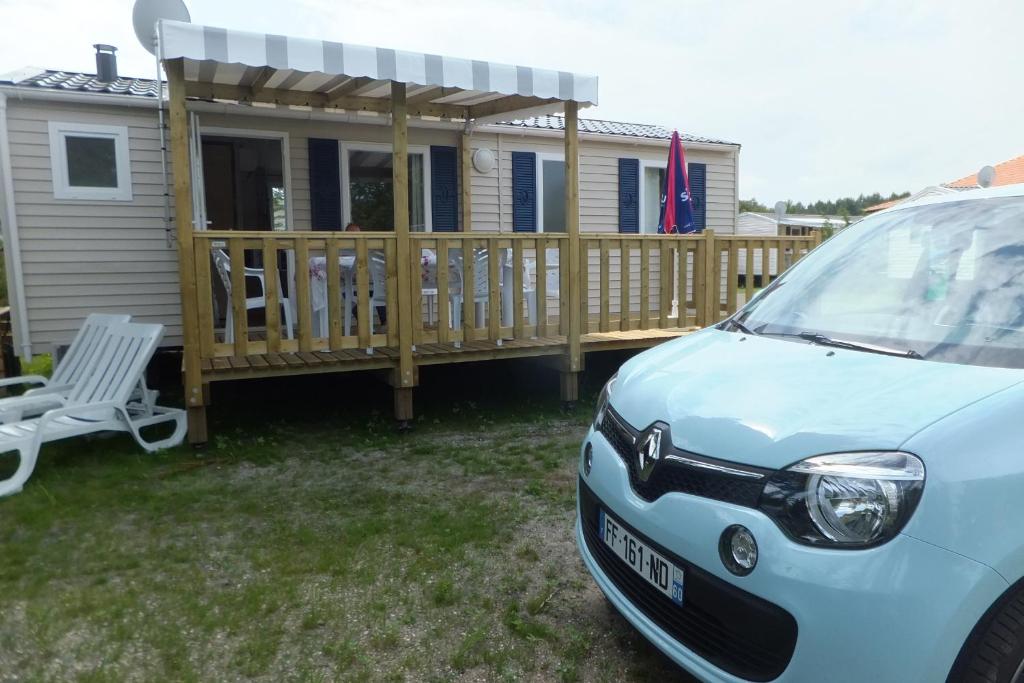 a car parked in front of a house with a deck at Mobil Home Confortable 873 Camping Siblu La Reserve in Gastes