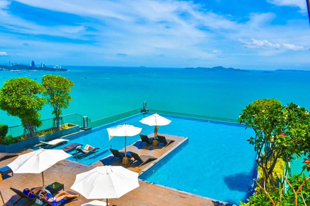 einen Pool mit Sonnenschirmen und dem Meer in der Unterkunft Wongamat Tower Condominium in Pattaya North