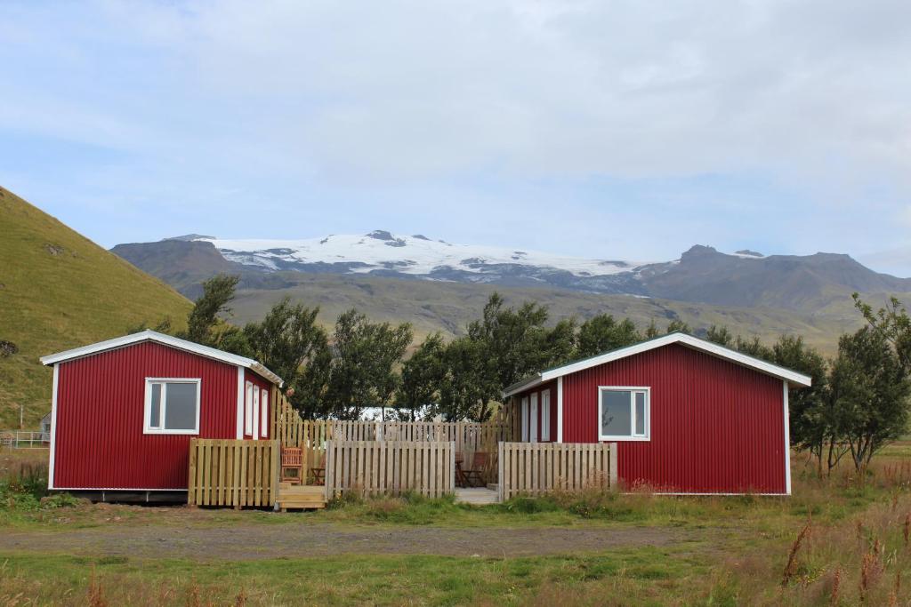twee rode huizen in een veld met bergen op de achtergrond bij Núpakot in Steinar