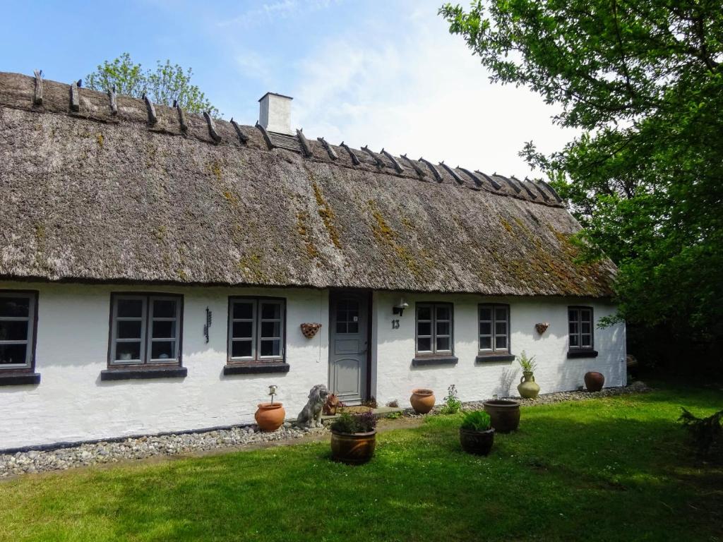 a white house with a thatched roof and potted plants at Feriehus stråtækt bindingsværksidyl in Maribo