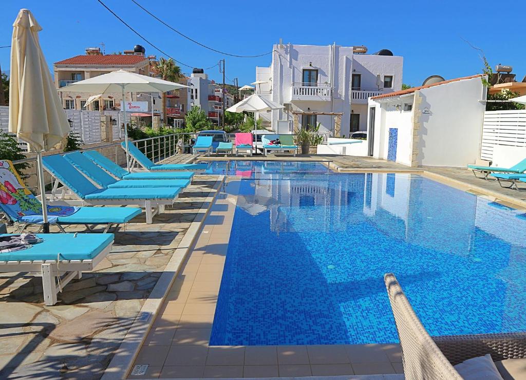 una piscina con sedie a sdraio e ombrelloni blu di Sonio Beach - Que Bella Collection a Plataniás